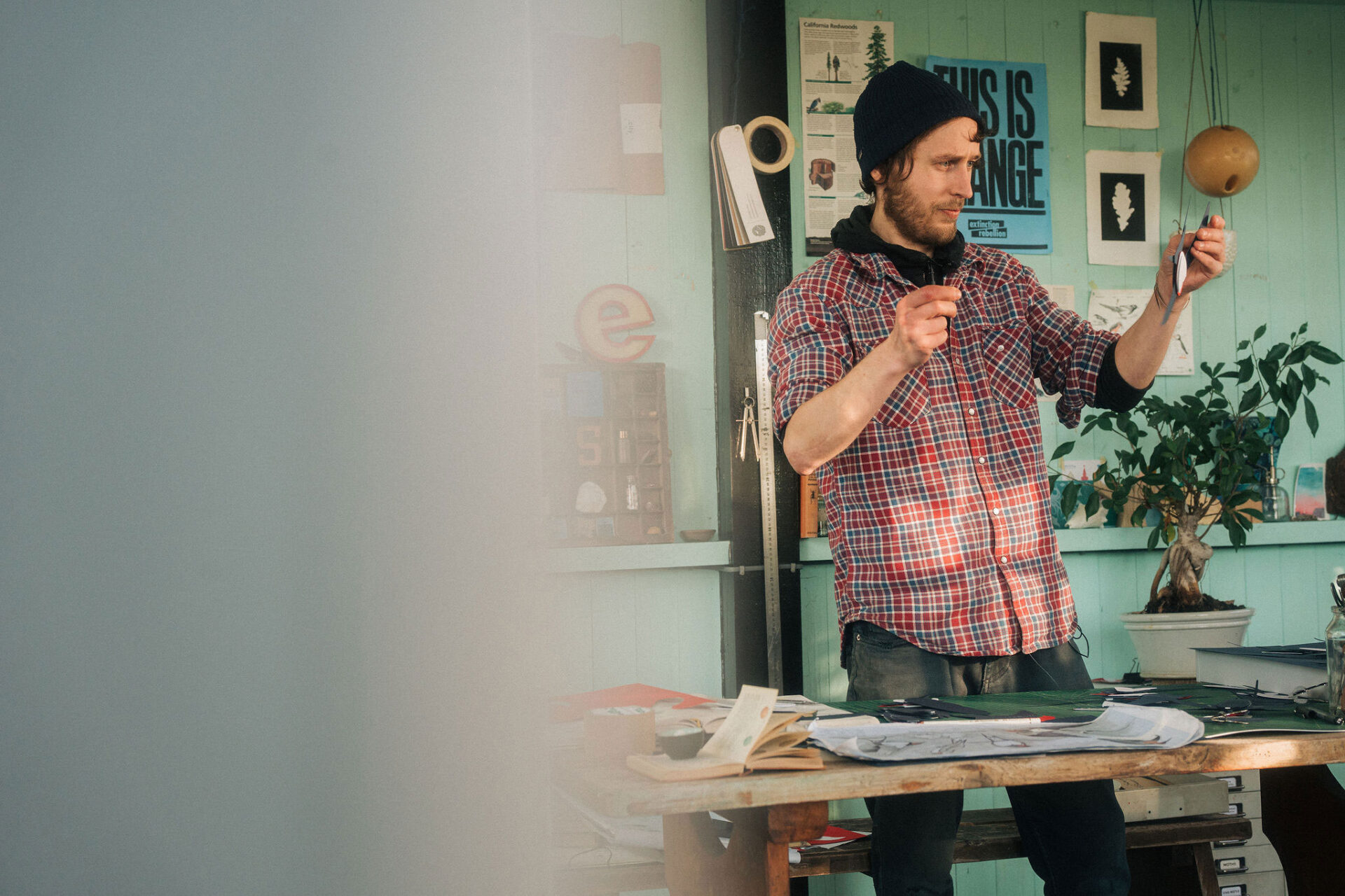 An artist standing in his studio holding up a paper bird.