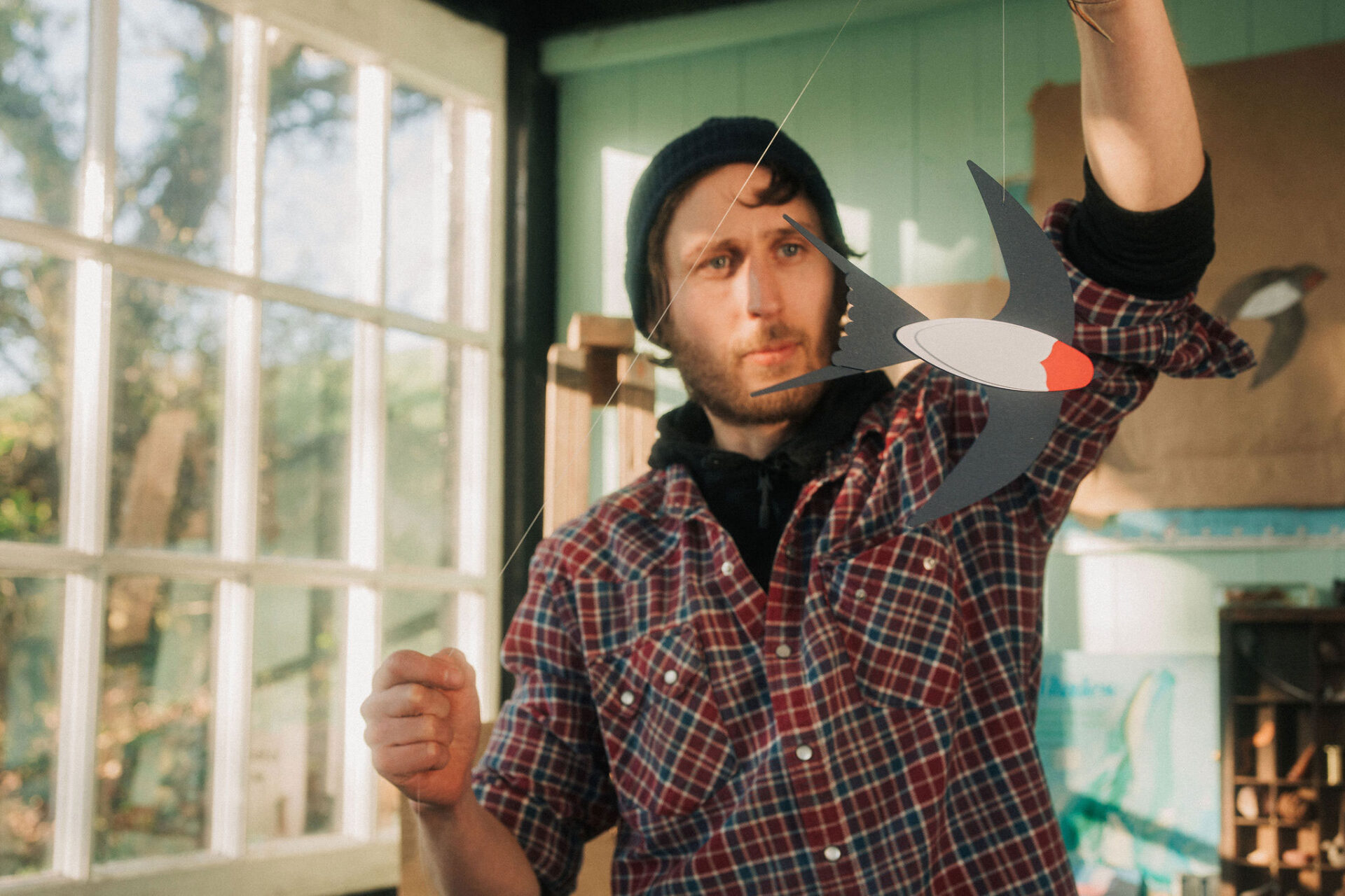 Artist hanging a papercut barn swallow by a thread in a studio.