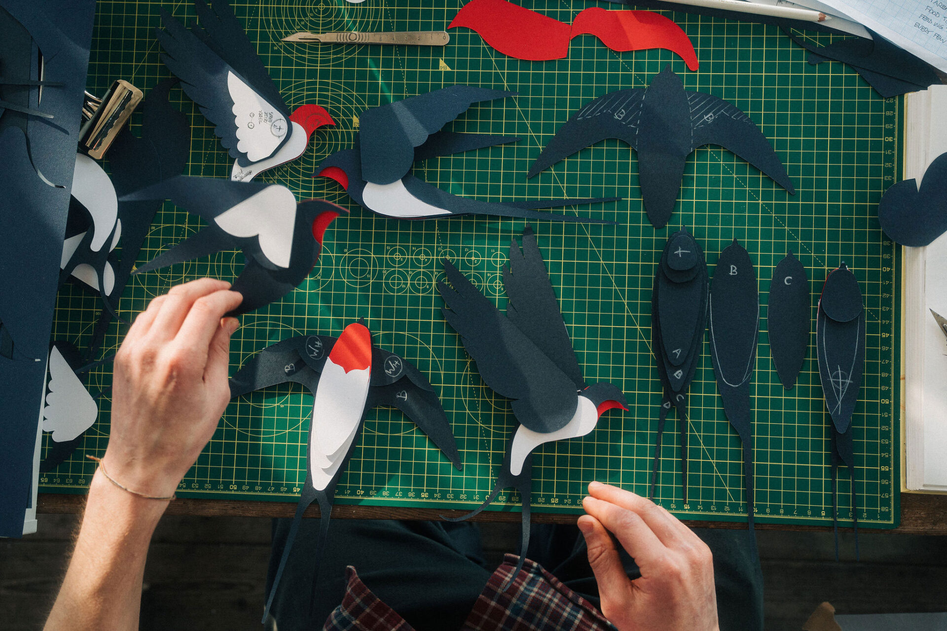 Overhead view of artist Ed Harrison in the studio assembling papercut barn swallows.