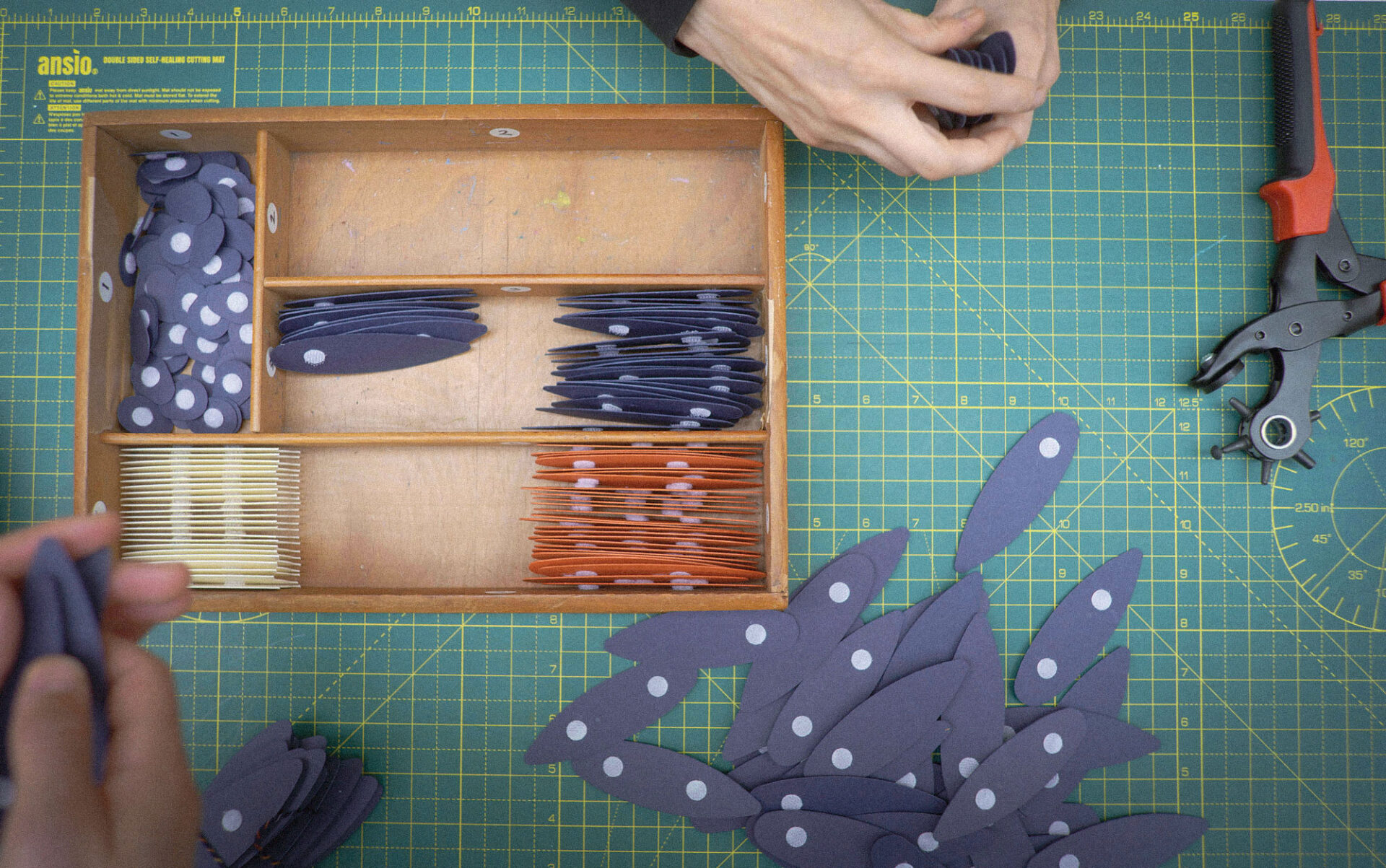 A pair of hands prepare components for paper birds on a desk for a craft workshop.