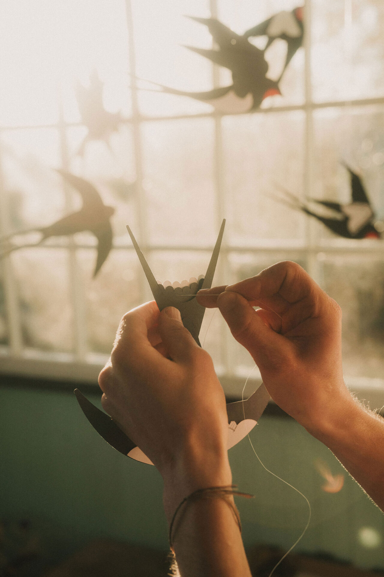 An artist threading a paper Barn Swallow in the studio