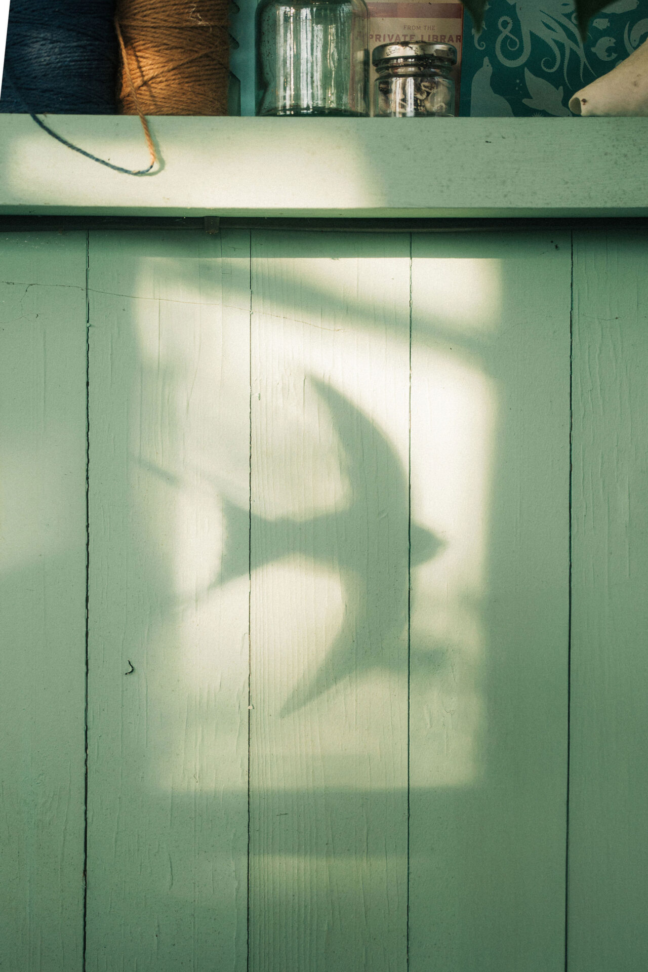 The shadow of a paper barn swallow is cast on a wooden wall.