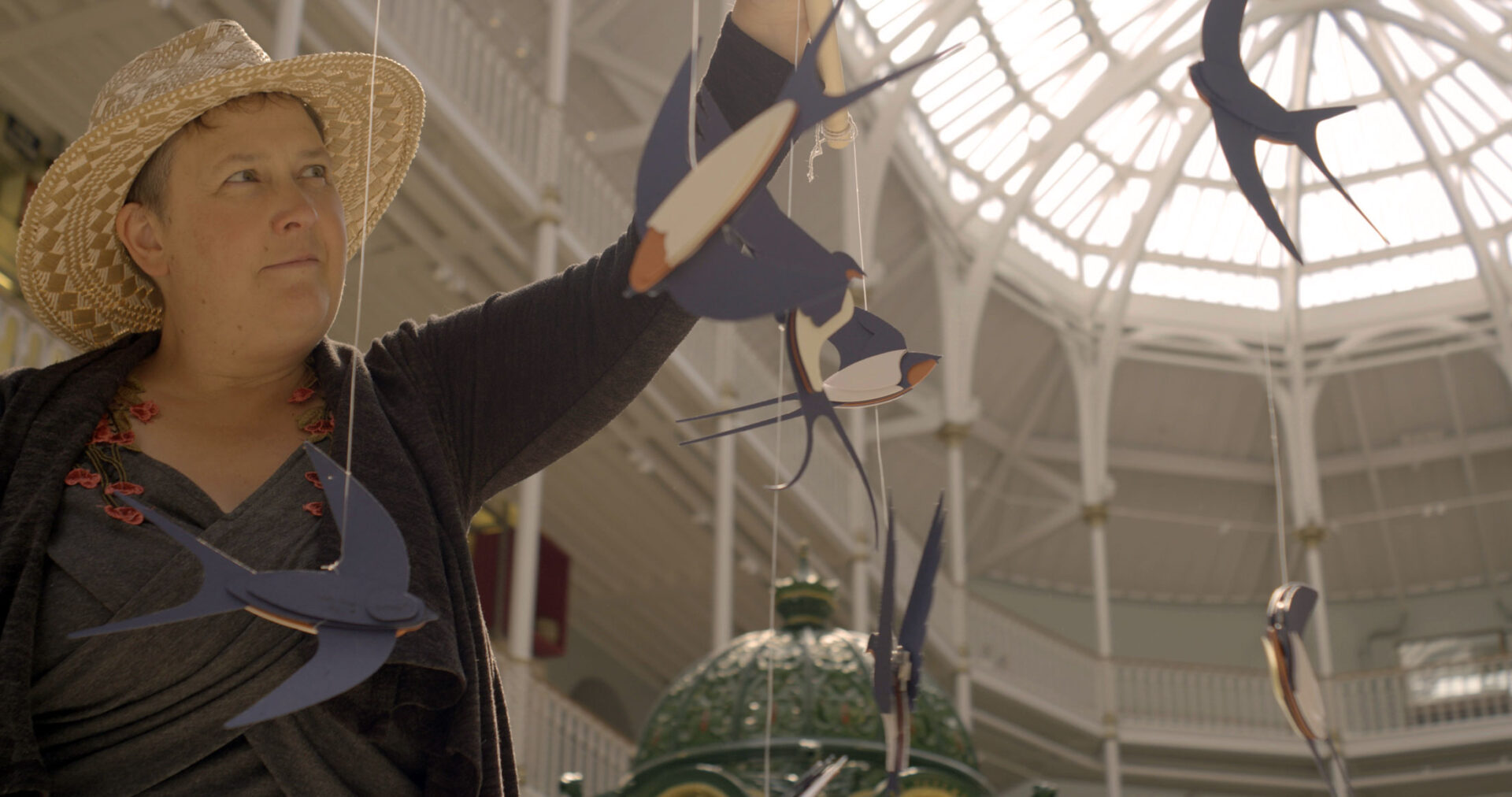 Storyteller holding a papercut barn swallow mobile inside a museum gallery.