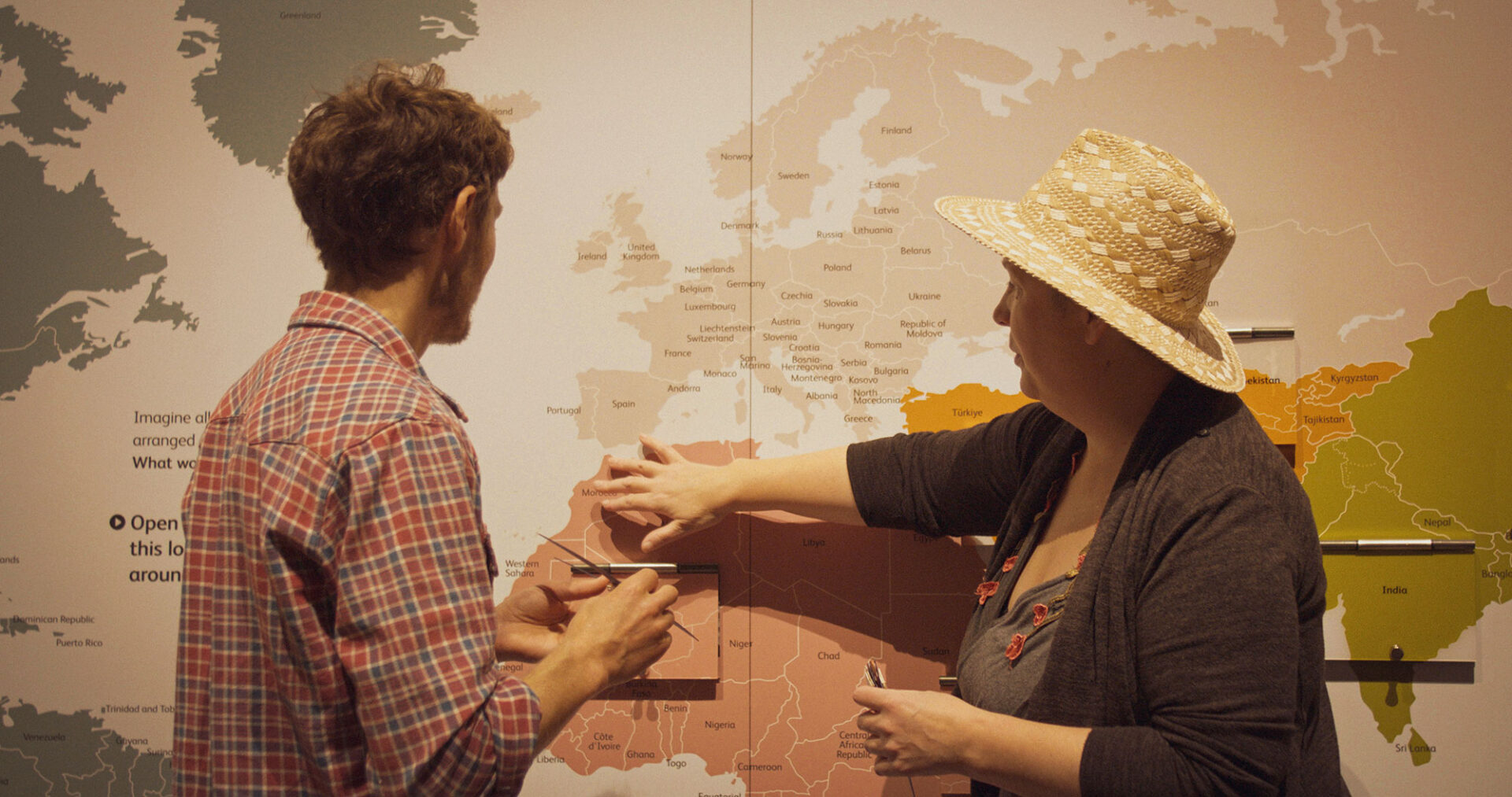 Artist and storyteller standing in front of a world map, tracing a migration route between the UK and Africa.