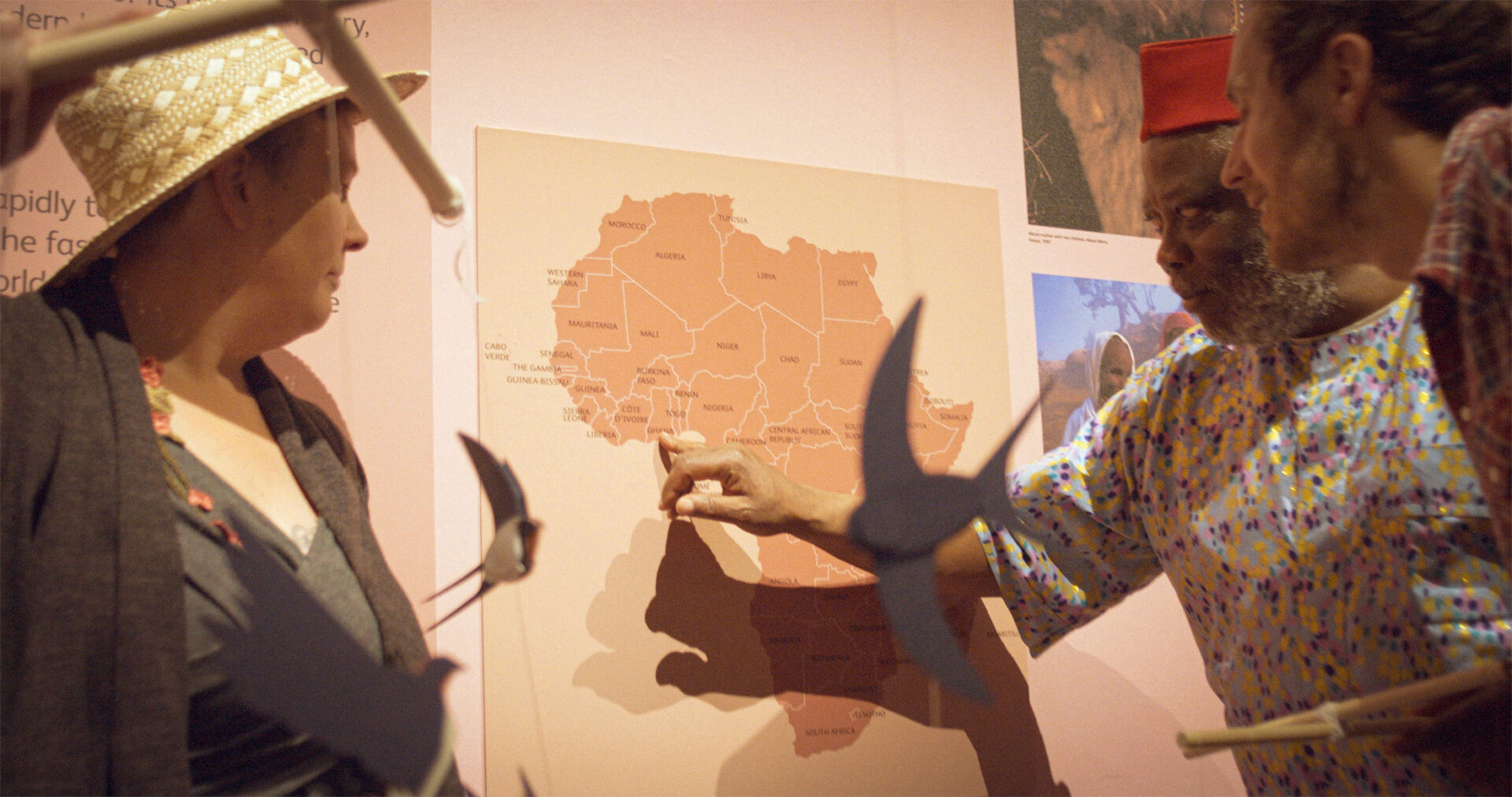 Storyteller points to Ghana on a map of Africa inside a museum gallery.