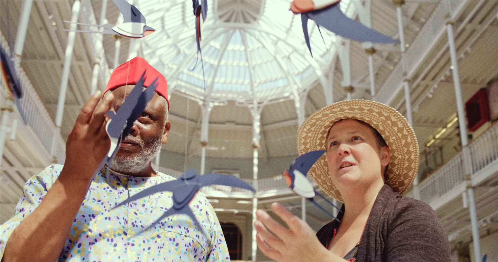 Two storytellers looking at a mobile of paper barn swallows inside a museum gallery.