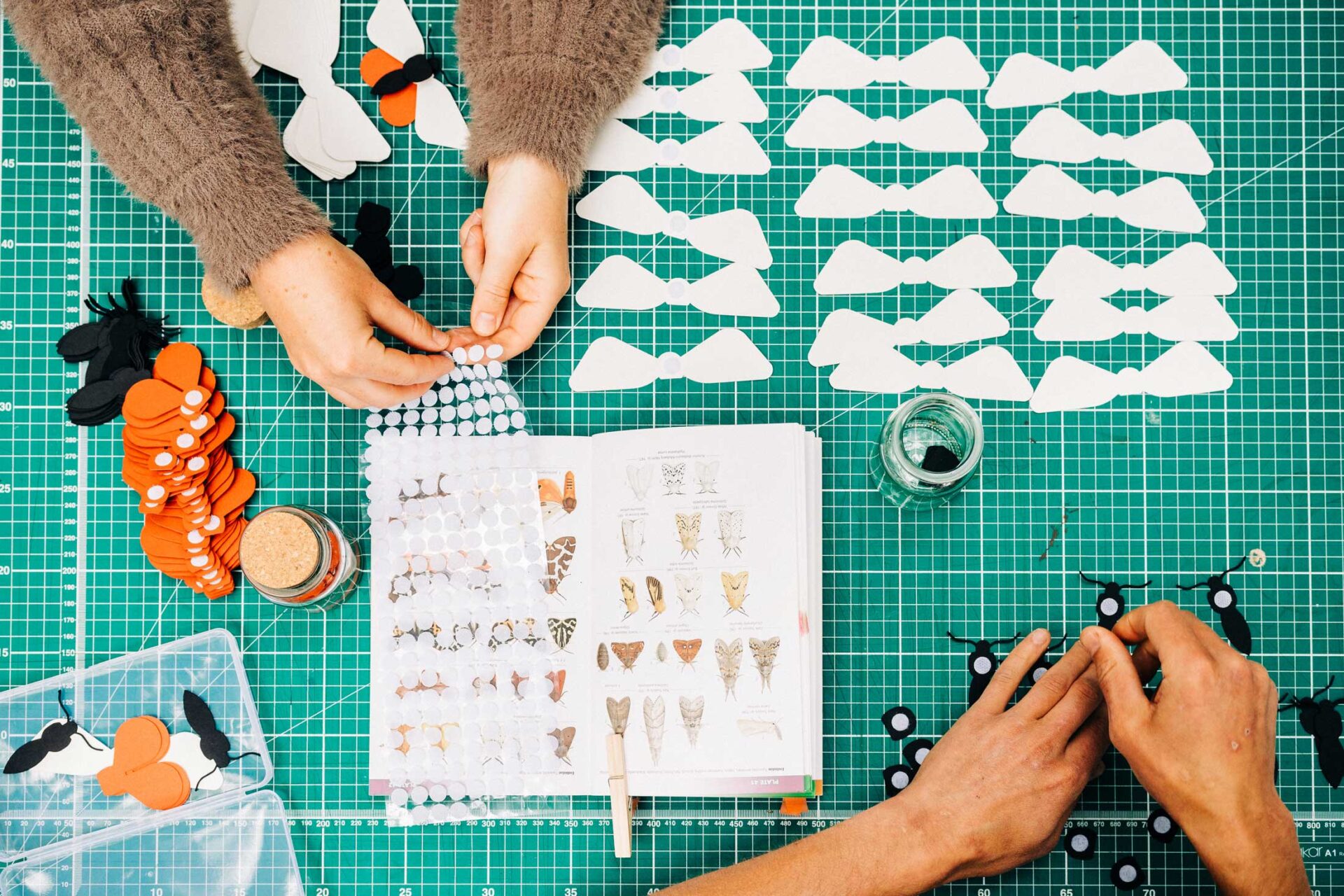 Two pairs of hands assembling paper butterfly models