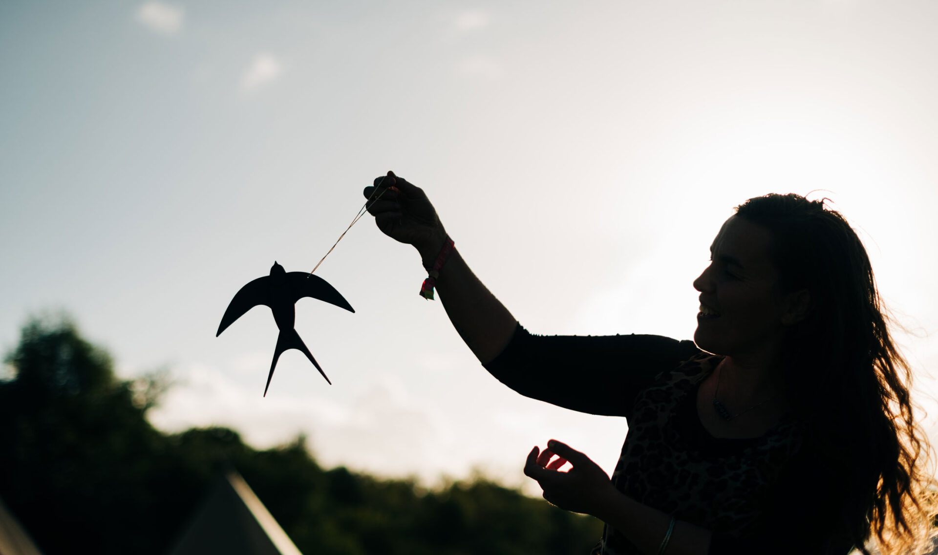 Female workshop participant holding a papercut barn swallow against a bright sky.