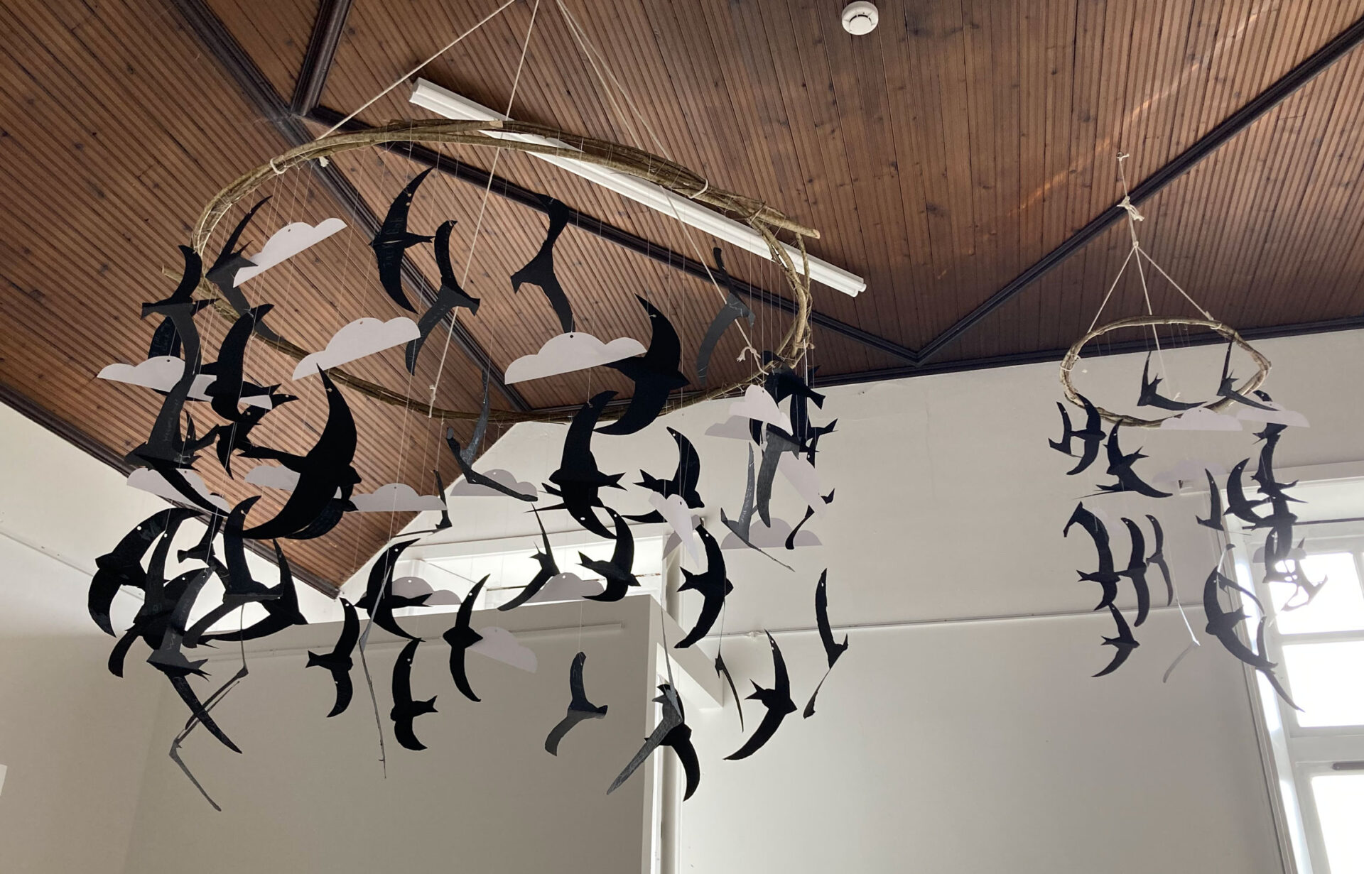 Two bird mobiles made from woven hazel hoops and suspended in a gallery.