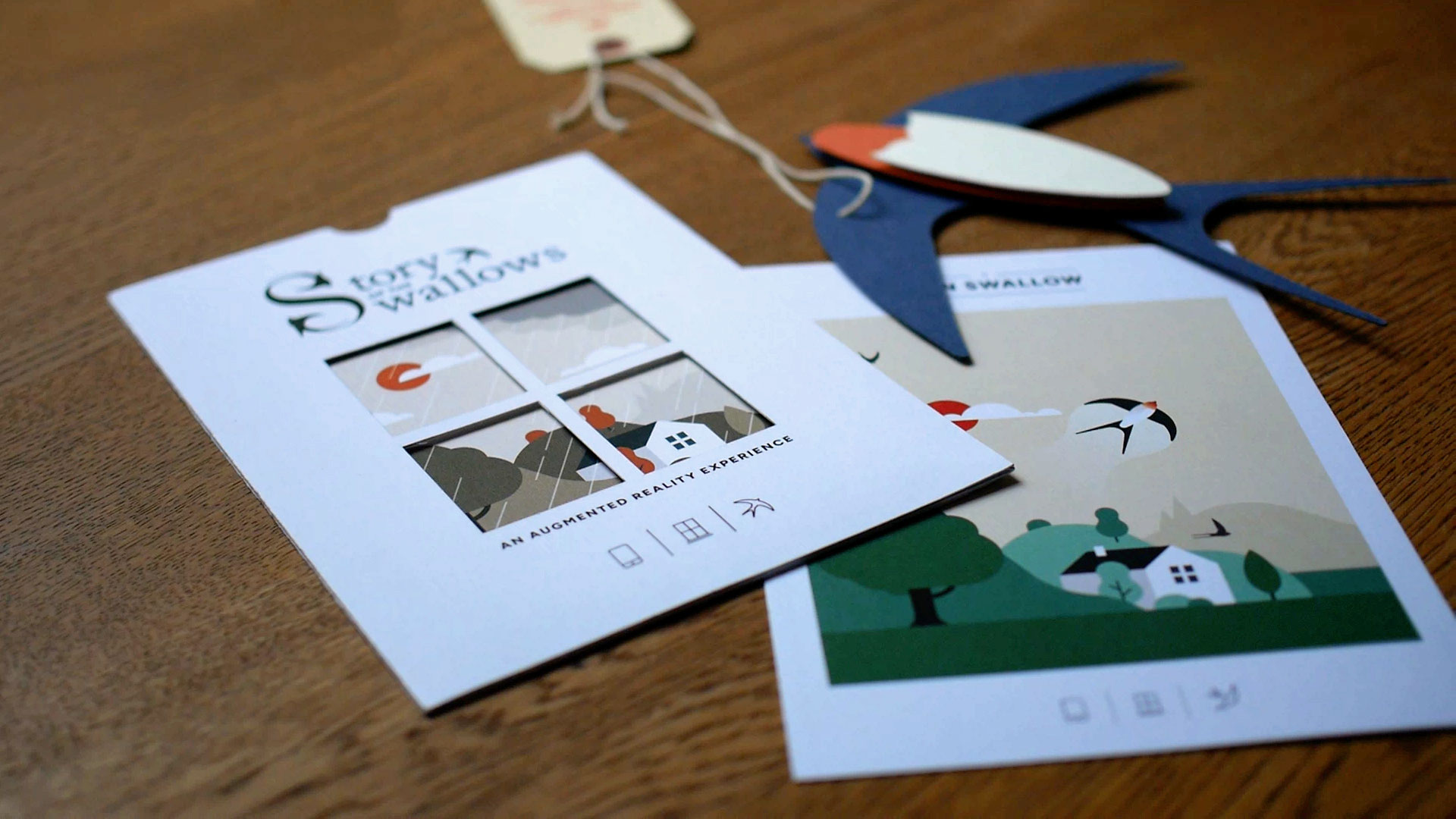 An AR postcard, packaging and an assembled paper barn swallow arranged on a wooden desk for Wild Wings of Hope.