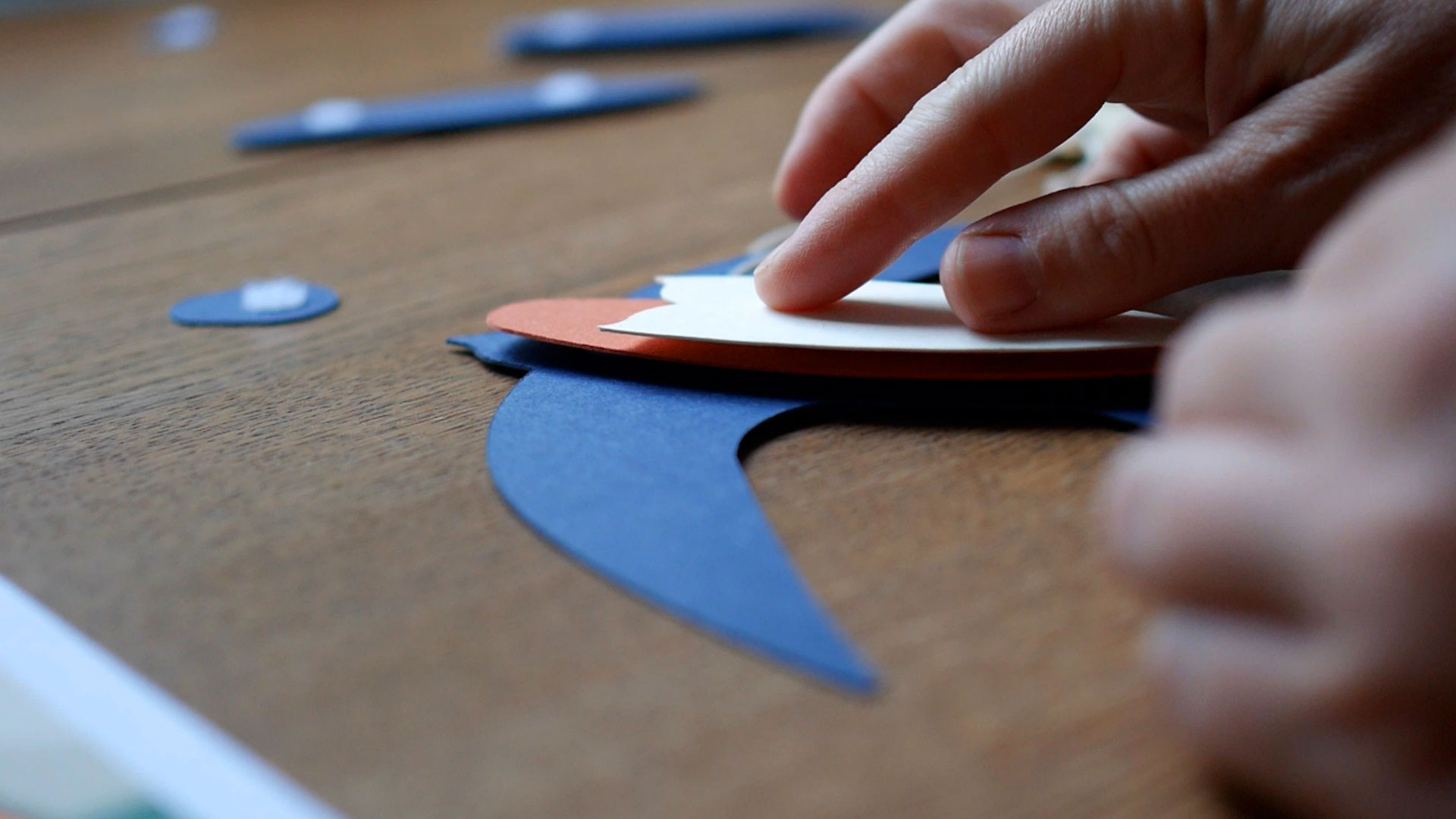 Hands assembling a paper barn swallow on a wooden desk.