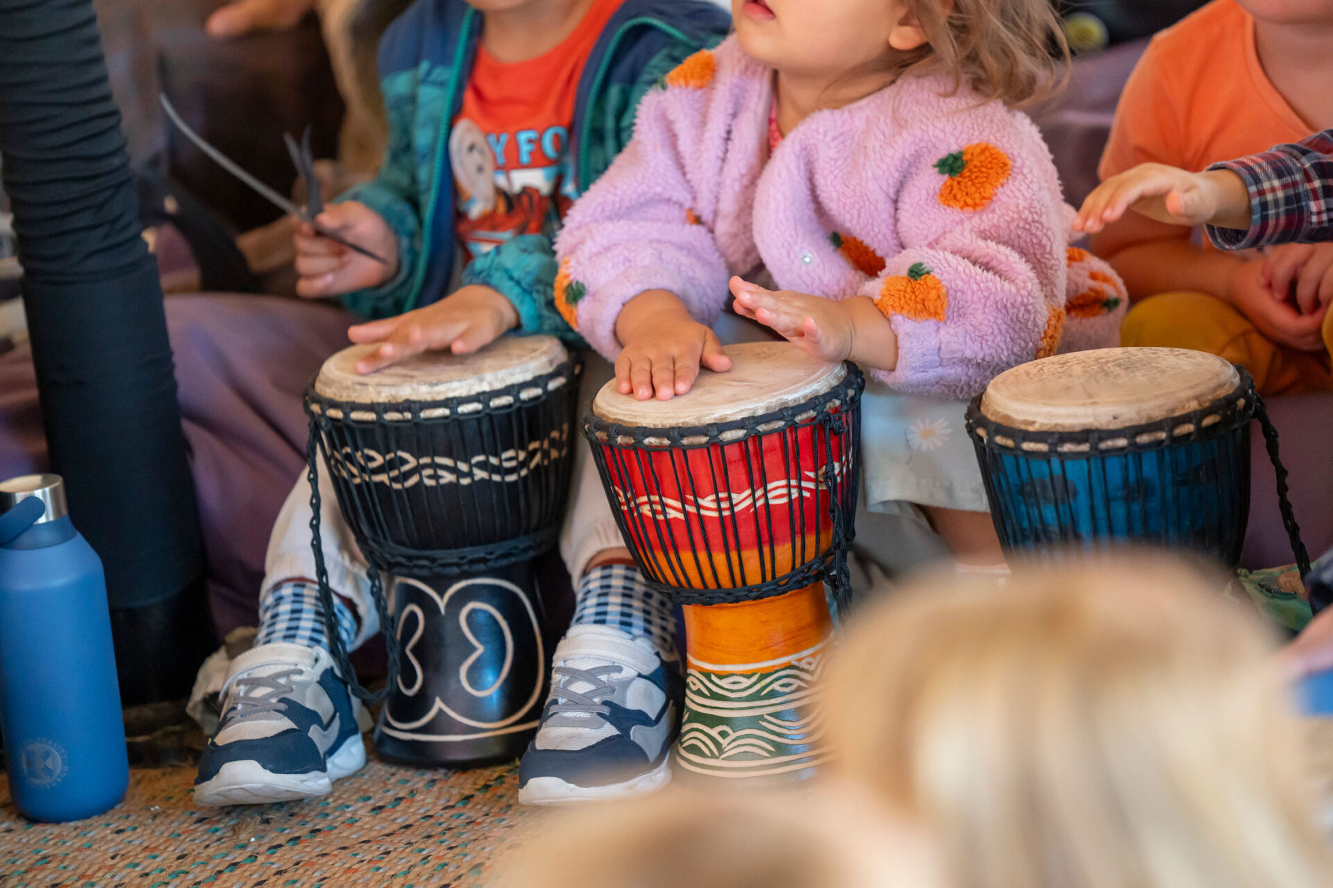 Close-up of children’s hands playing bongo drums together in a participatory drumming circle at the Edinburgh International Book Festival.