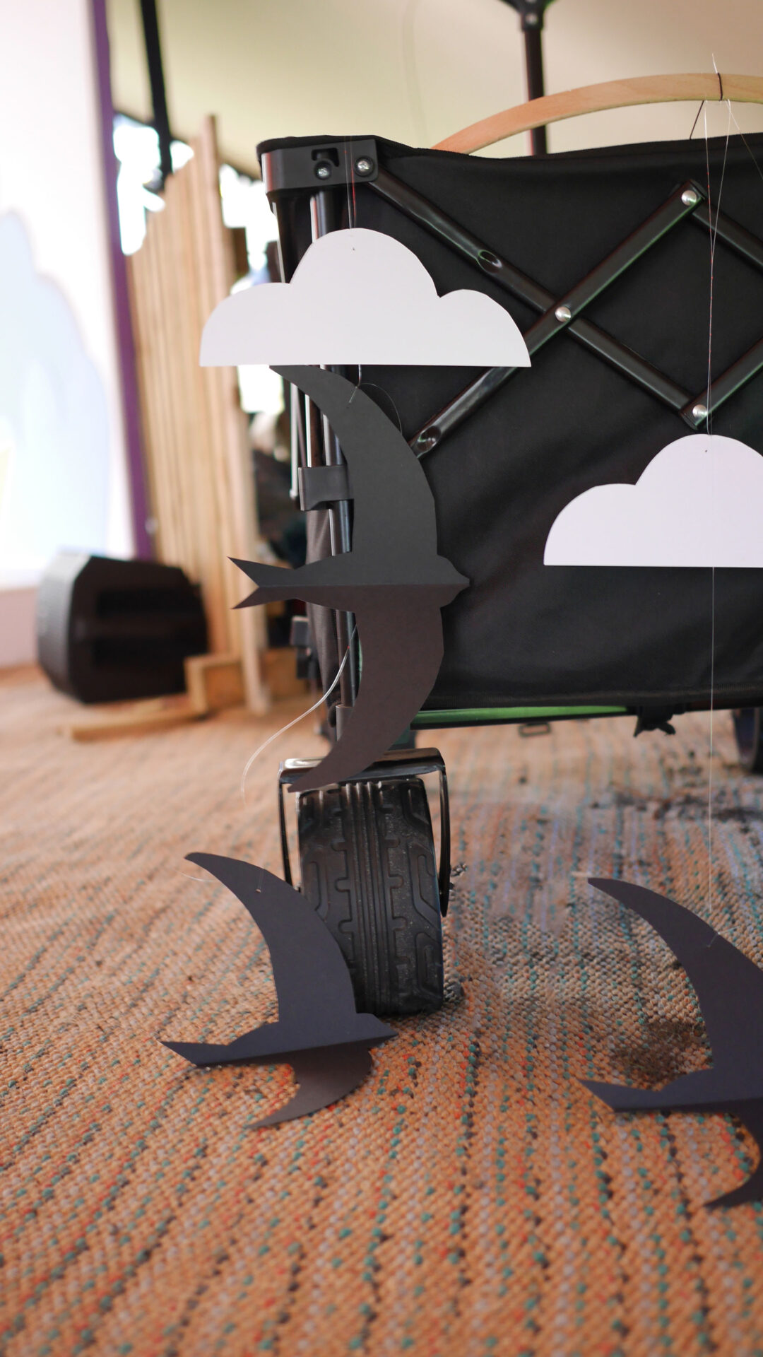 A black festival trolley with a mobile of paper swifts and clouds hanging off it.