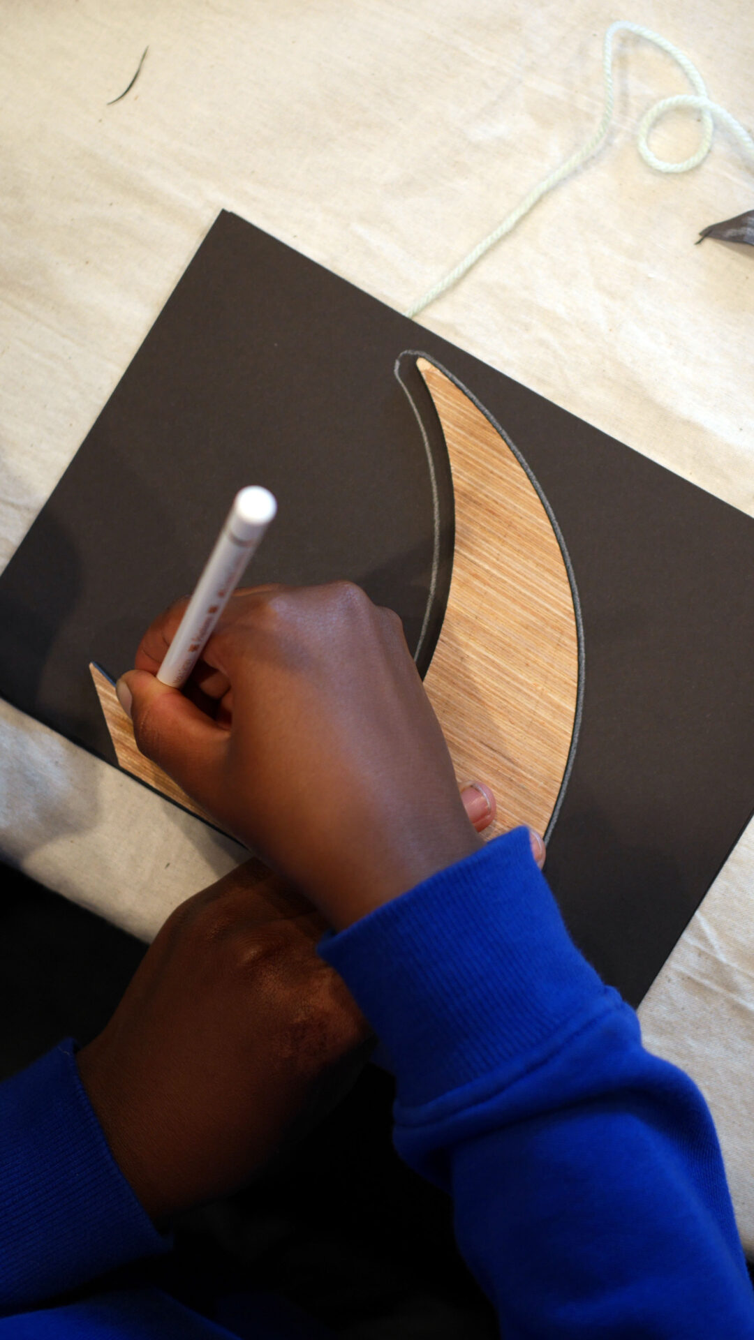 A child drawing a paper swift using a wooden stencil on black card.