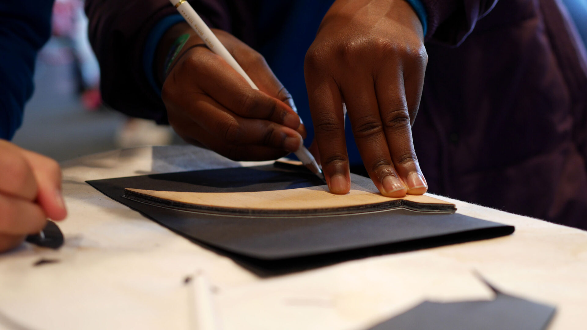 A child drawing a paper swift using a wooden stencil on black card.
