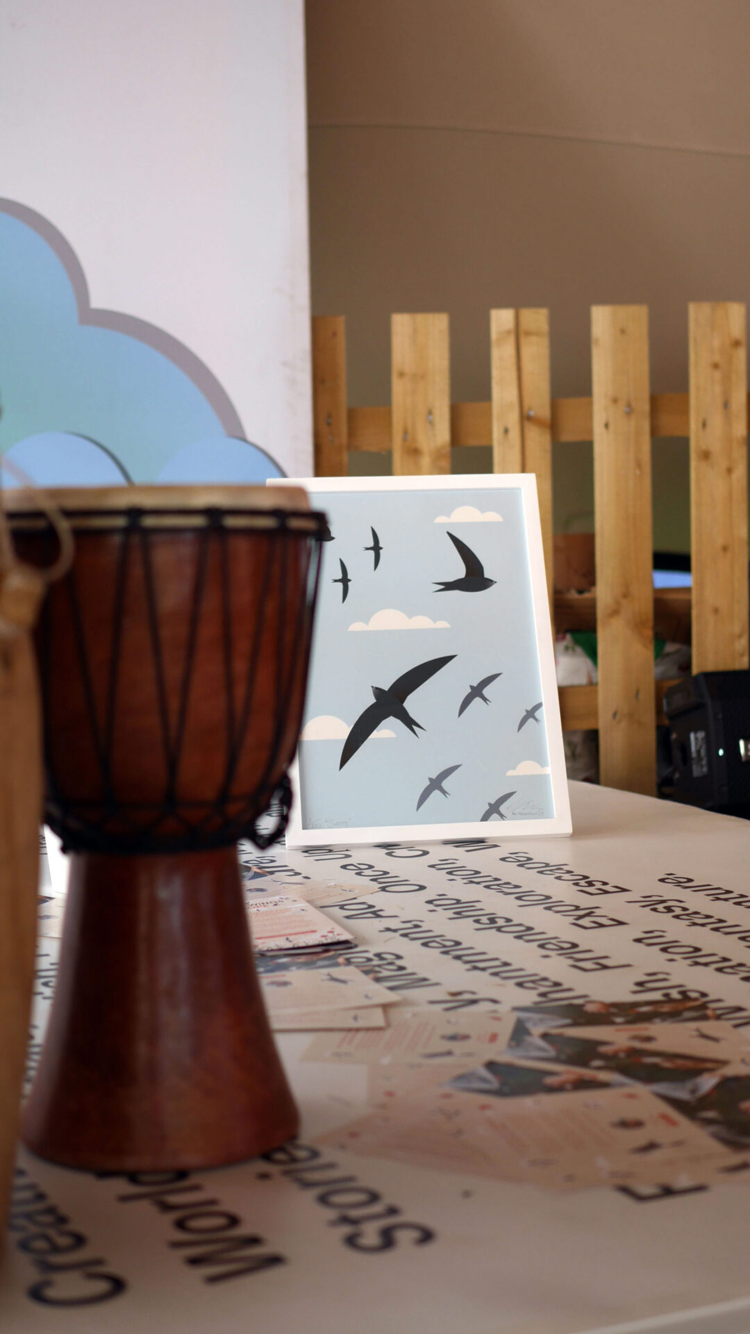 A framed piece of artwork of Swifts on stage behind two traditional African hand drums.