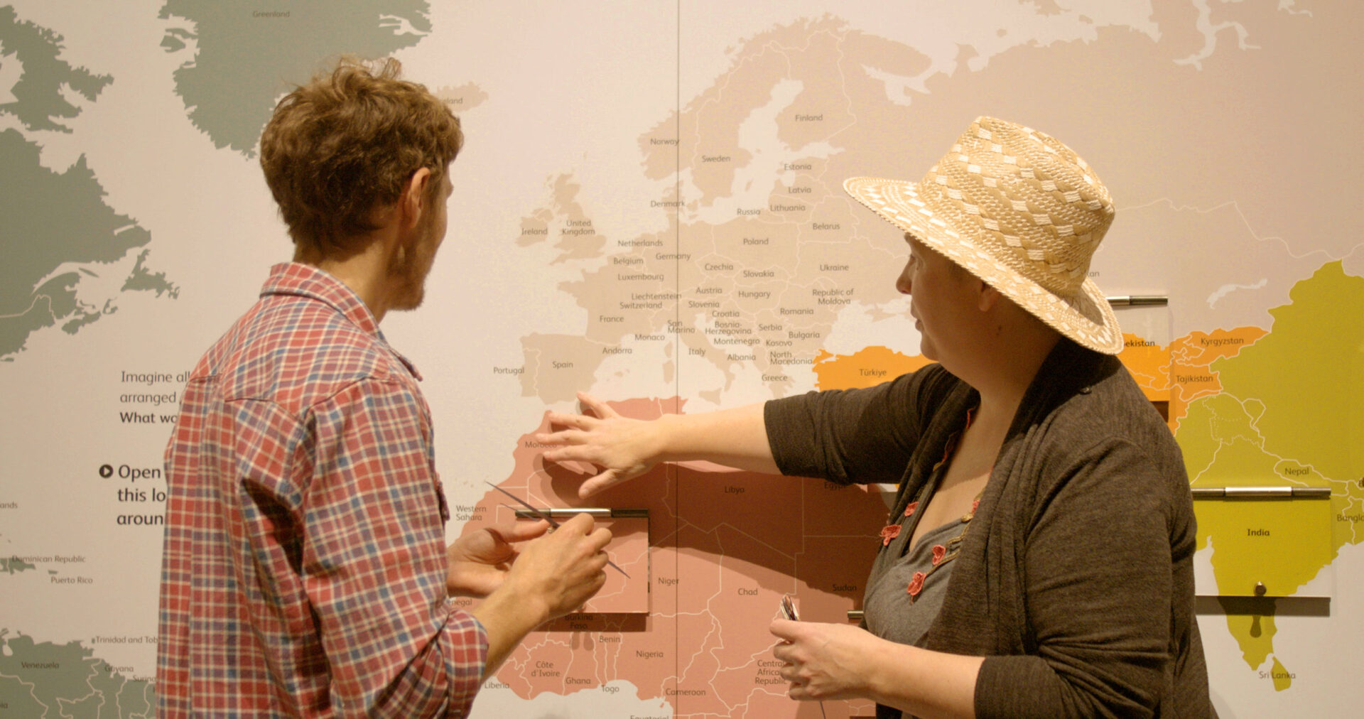 Ed Harrison and Cara Silversmith talking and pointing at a large world map.